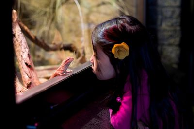 Side view of girl looking at reptile through window at home