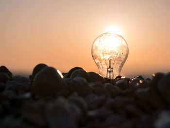 Low angle view of illuminated light bulb against sky during sunset