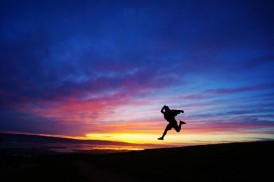 Silhouette of woman jumping in sea at sunset