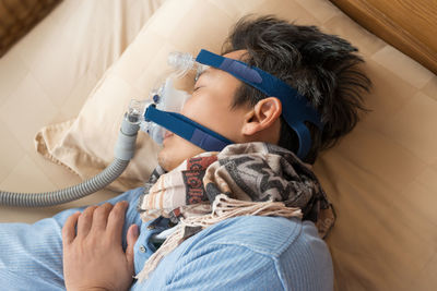 High angle view of mature man wearing oxygen mask while sleeping on bed