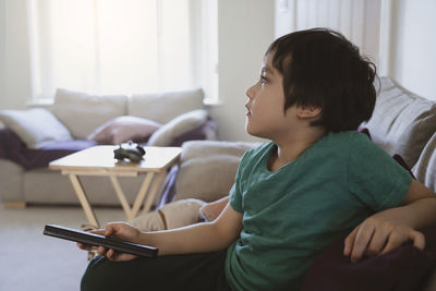 Kid lying on sofa holding remote control and watching cartoon on tv with morning light,child boy 
