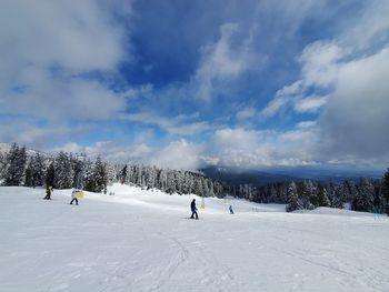 People skiing on snow covered mountain against sky