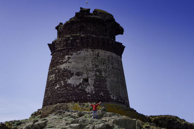 Hiker with arms outstretched standing by old ruin against clear blue sky