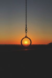 Chain and pendant hanging against sea during sunset