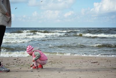 Girl standing by mother on shore at beach against sky