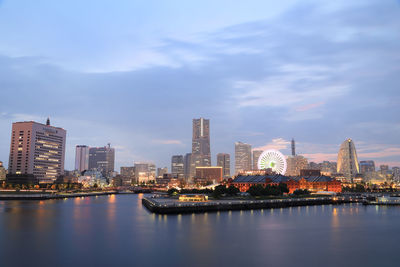 Illuminated buildings by river against sky in city