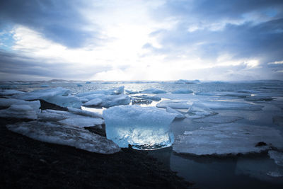 Icebergs at beach against cloudy sky