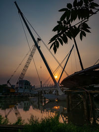Cranes at harbor against sky during sunset