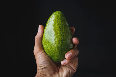 Close-up of hand holding apple against black background