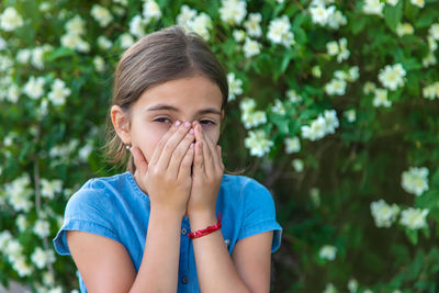 Sick girl sneezing against plant