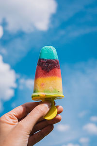 Cropped hand holding ice cream cone against sky