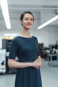 Smiling businesswoman with hands clasped standing in industry