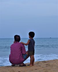 Rear view of boys on beach against sky
