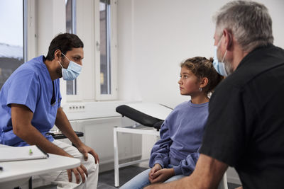 Male doctor talking to girl patient and grandfather during appointment