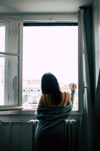 Rear view of woman looking through window at home