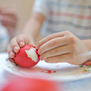 Hands of a child peeling red boiled egg