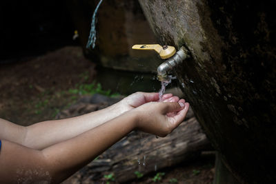 Cropped image of child with hands cupped on faucet