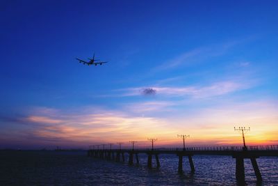 Airplane flying over sea against sky during sunset