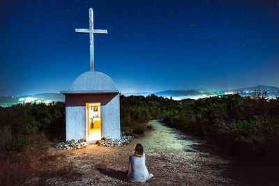 Rear view of woman looking at cross against blue sky