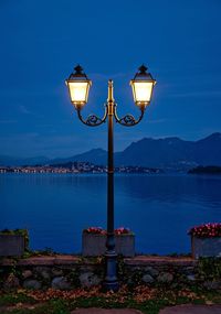 Illuminated street light by sea against sky at night