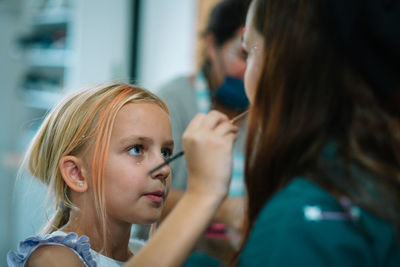 Portrait of little girl putting makeup on her mother