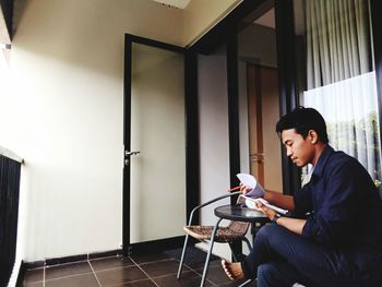 Side view of man reading document while sitting at home