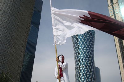 Low angle view of woman holding flag against buildings in city