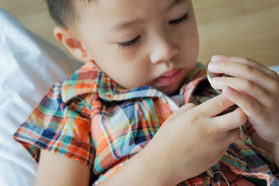 High angle view of cute boy holding clock while lying at home