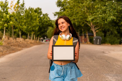 Smiling woman holding digital tablet while standing on road