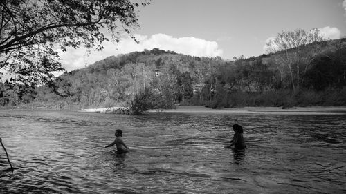 Mother and daughter crossing river against tree mountains