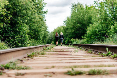 Rear view of people on railroad track amidst trees