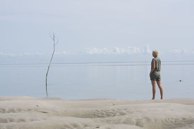 Rear view of woman standing on beach against sky