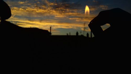 Silhouette man holding camera against sky at sunset