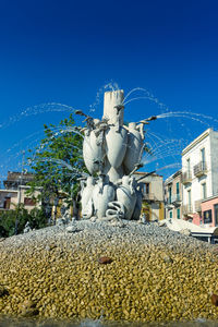 Statue by fountain in city against clear blue sky