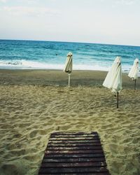 Deck chairs on beach against sky
