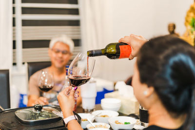 Woman hand pouring red wine into a glass from bottle at dinner party.