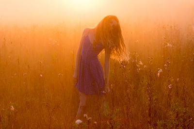 Woman standing on field against sky during sunset