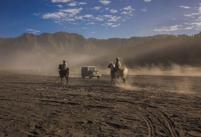 People riding horses on land against sky