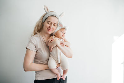 Mom blonde and newborn daughter in white with rabbit ears photo on a light background