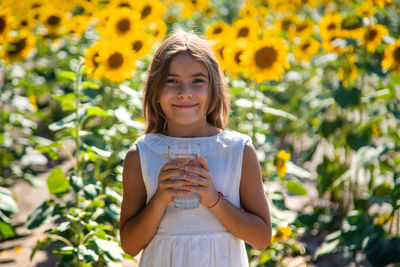 Portrait of cute girl holding glass of water in sunflower field