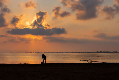 Silhouette woman standing on beach against sky during sunset