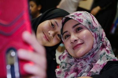 Young woman wearing hijab taking selfie with friend from mobile phone