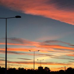 Low angle view of silhouette street lights against orange sky