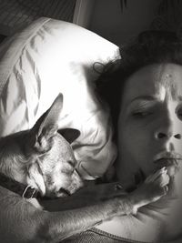 High angle view of woman lying by dog with paw on her face at bed
