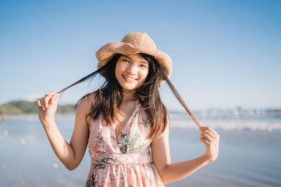 Portrait of smiling young woman in hat against sky