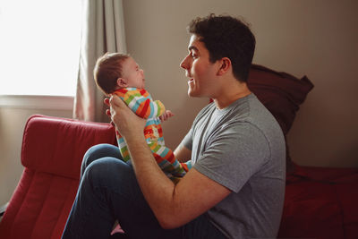 Side view of man holding baby boy at home