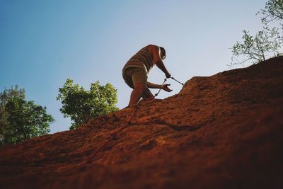 Low angle view of man climbing on rock against clear sky