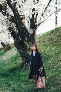 Full length of woman standing under cherry blossom tree while snowing