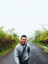 Portrait of smiling young man standing on road against sky