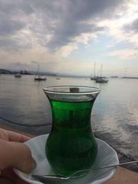 Cropped hand holding green drink at beach against sky